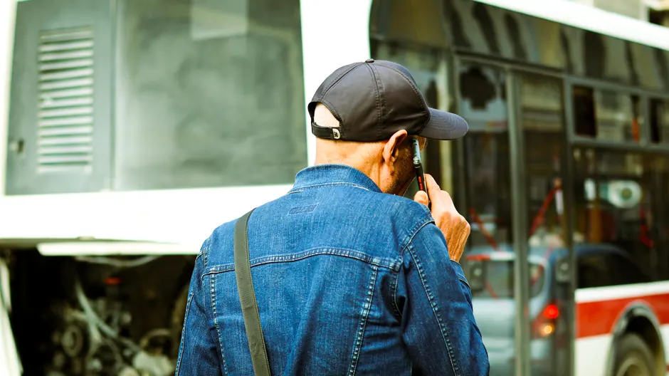 A man in a cap examines a broken-down bus on a city street.