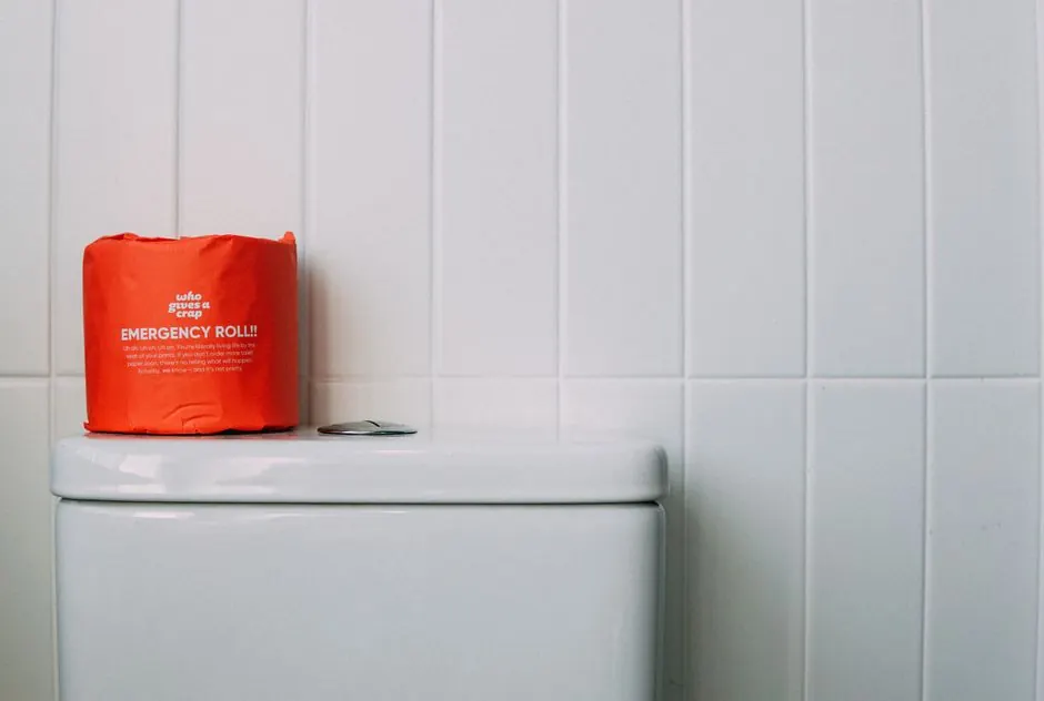 Minimalist bathroom scene featuring a red emergency toilet paper roll on a white toilet tank.